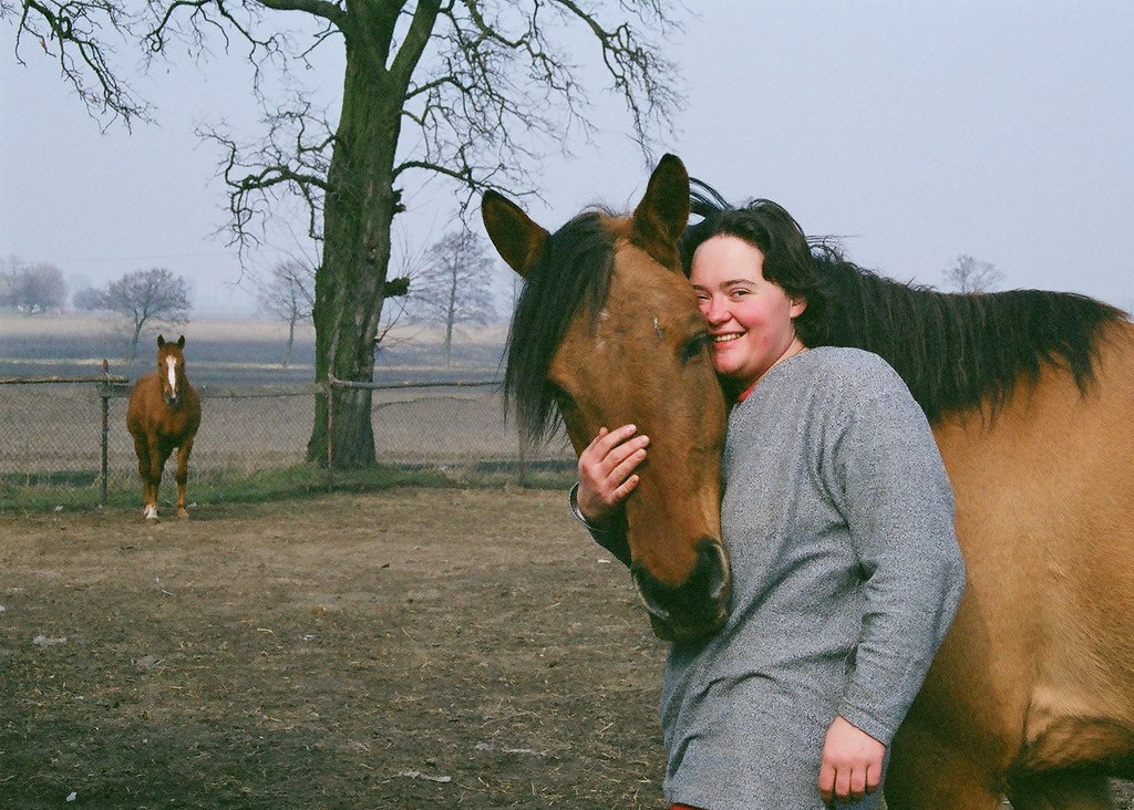 uśmiechnięta kobieta przytulająca się do pyska konia